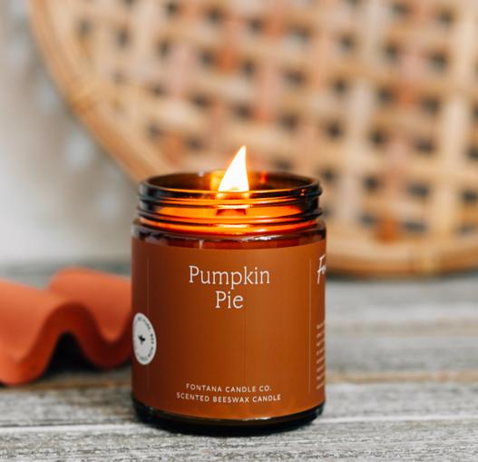 Pumpkin Pie scented candle in an amber jar with a wicker chair in the background.