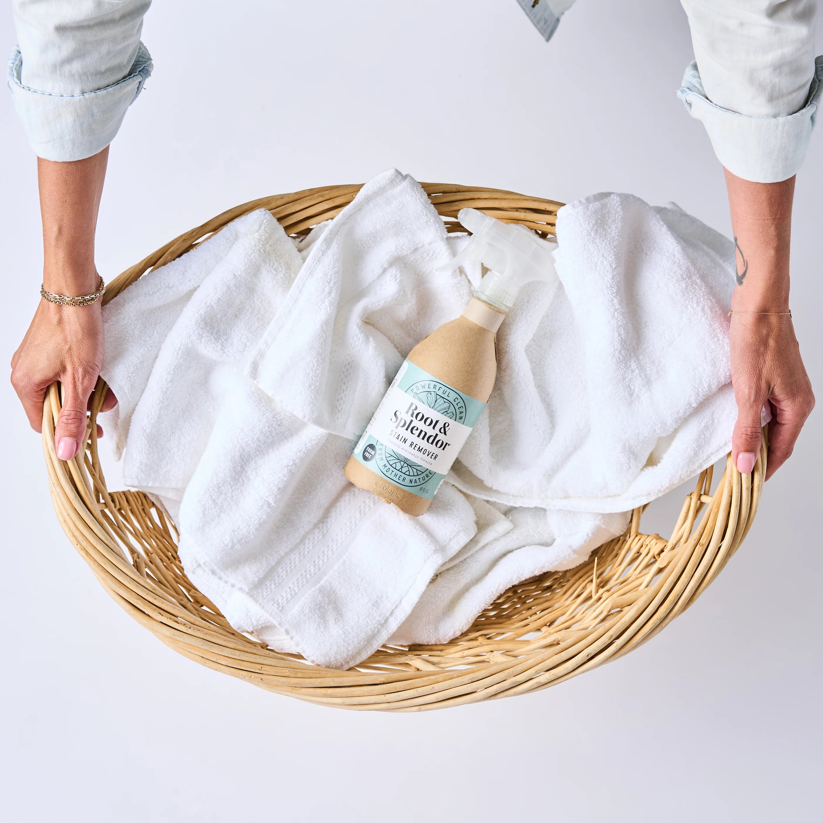 Two hands hold a wicker basket with white towels and a bottle of laundry detergent inside. The scene conveys cleanliness and freshness.