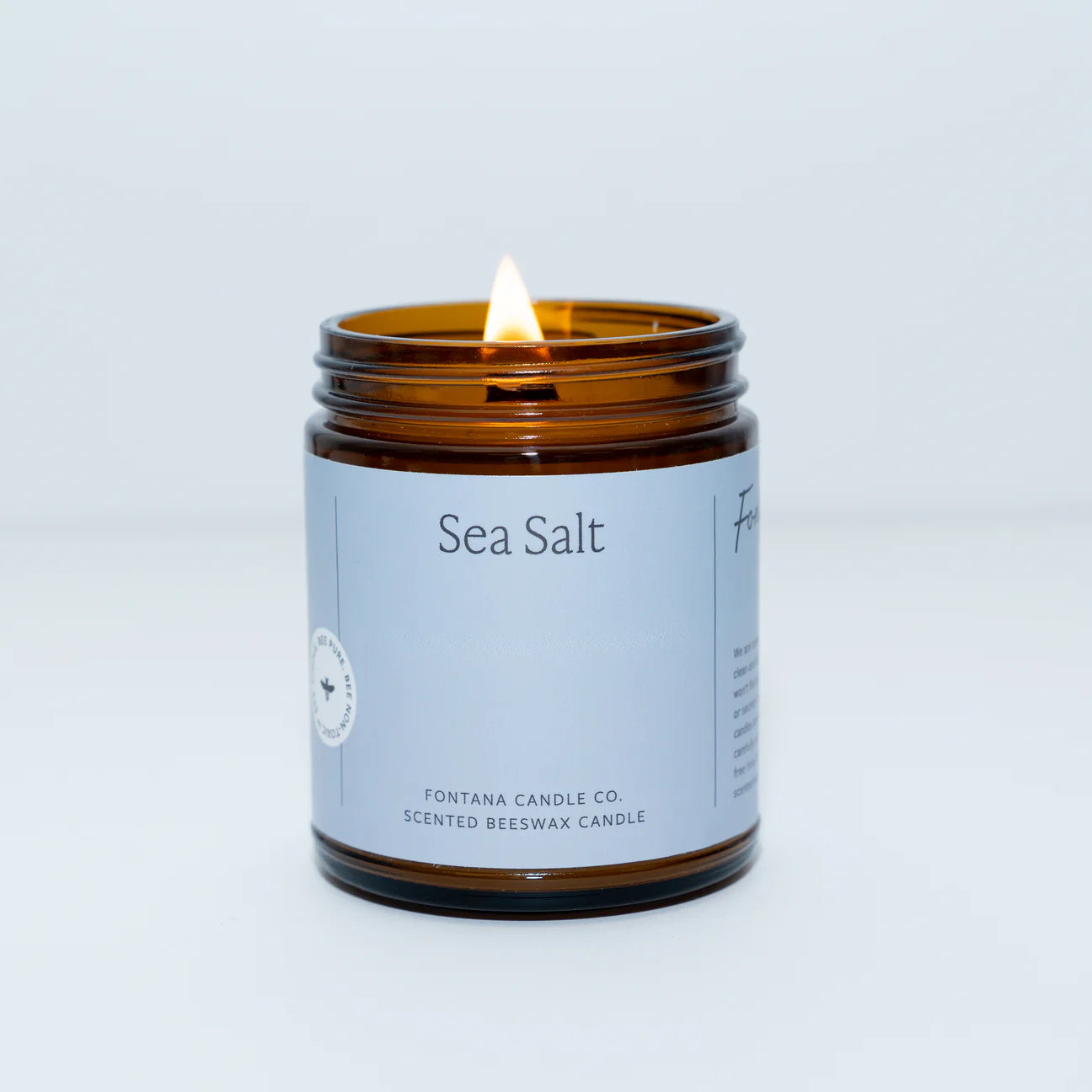 A lit Sea Salt scented essential oil candle in a clear glass jar with a blue label.