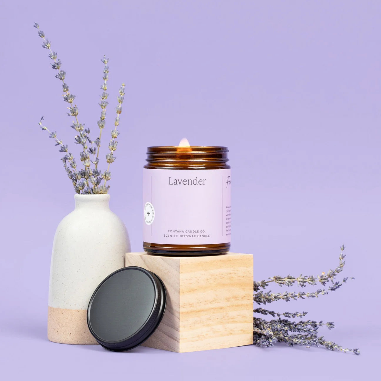 Lavender candle with a bottle of lavender oil and lavender flowers on a purple background