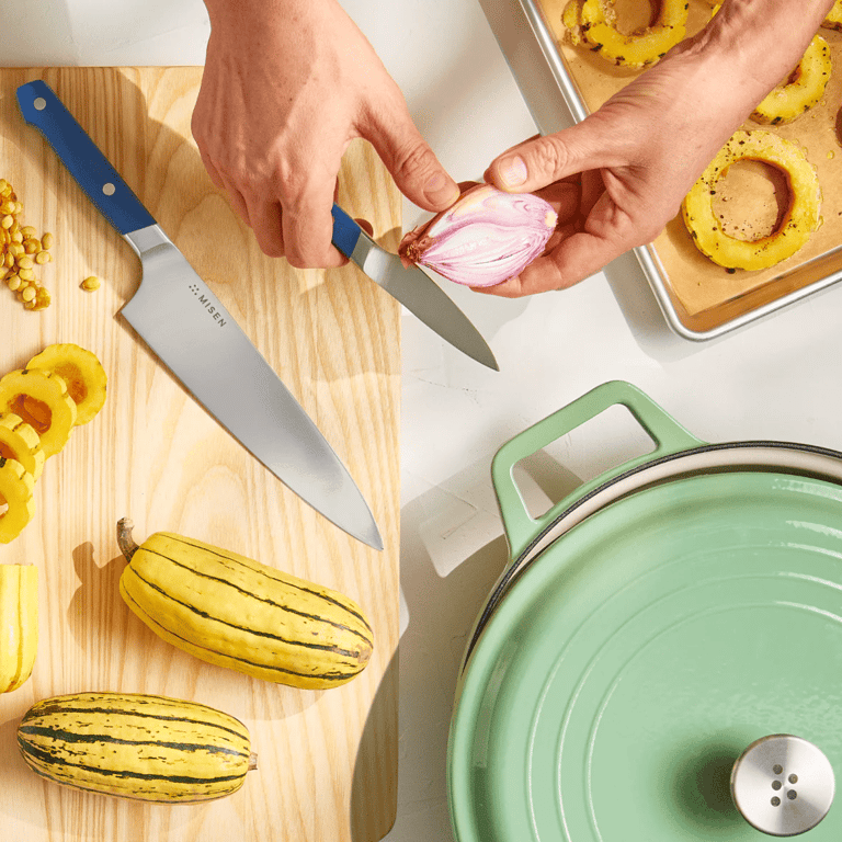 Person preparing food on a wooden cutting board with a knife cutting onion.